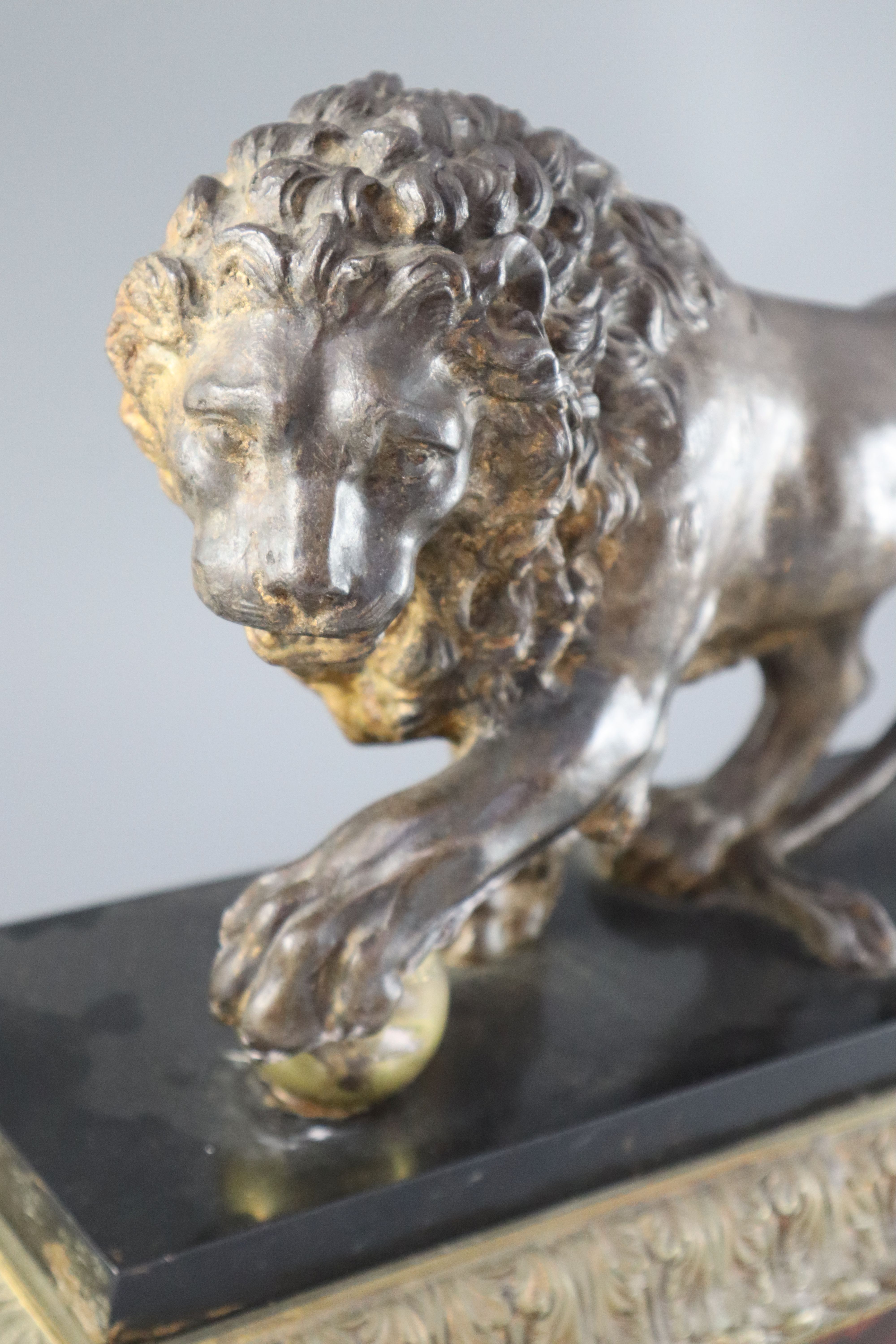 An early 19th century cast iron model of a lion standing with its foot upon a brass ball, width 15in. height 9.25in.